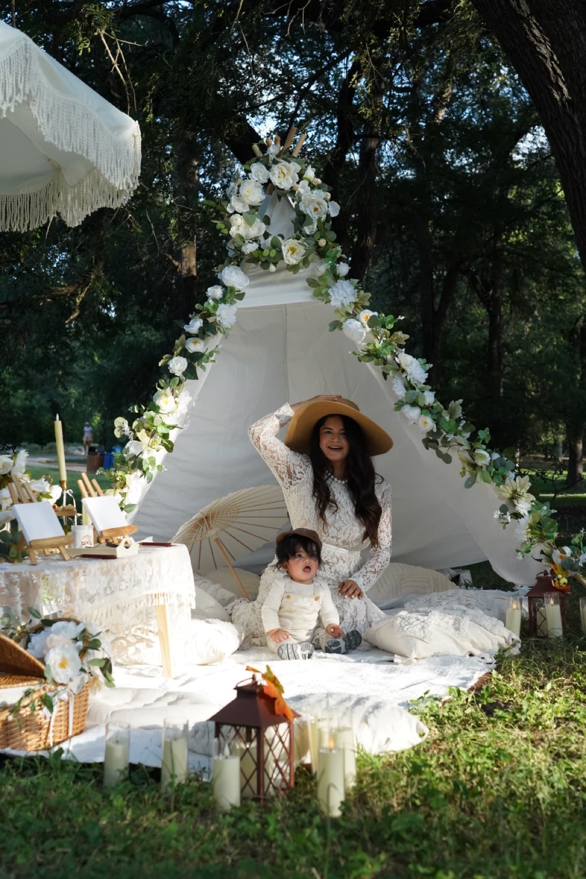 Mother and baby at a whimsical white boho picnic tent draped in flowers in Austin
