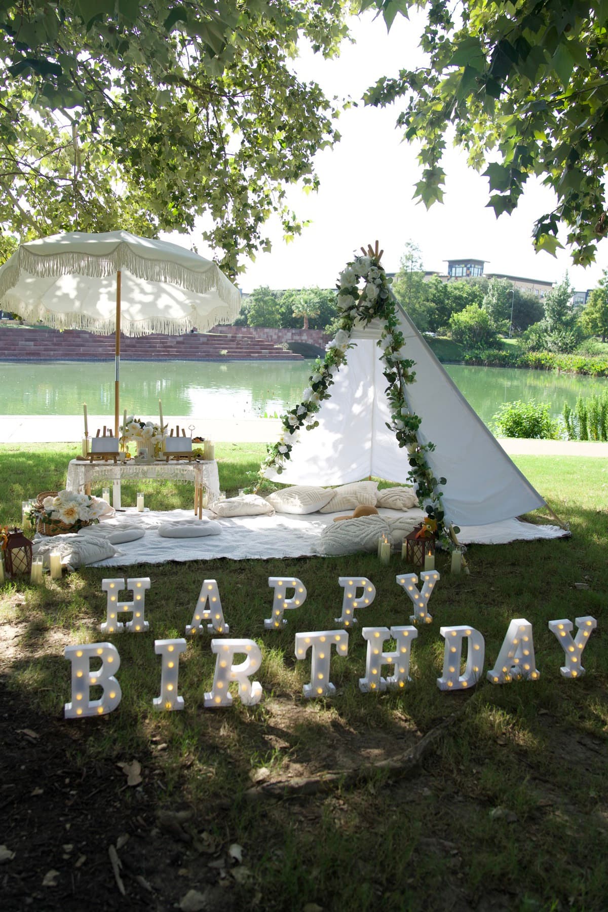 Happy Birthday picnic setup with a white tent, fringe umbrella and lake view in Austin